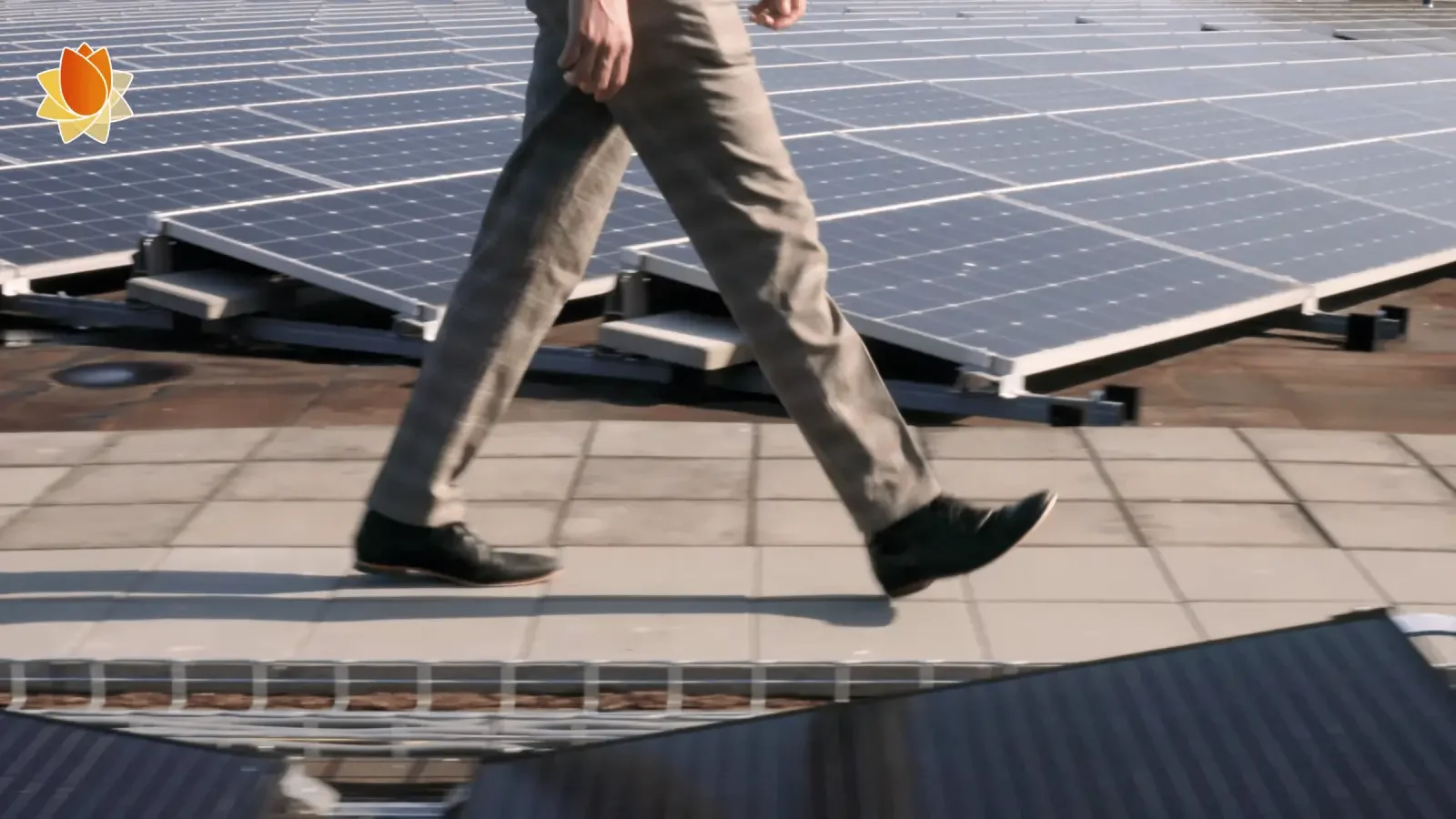 De benen van een man in pak die wandelt tussen rijen zonnepanelen